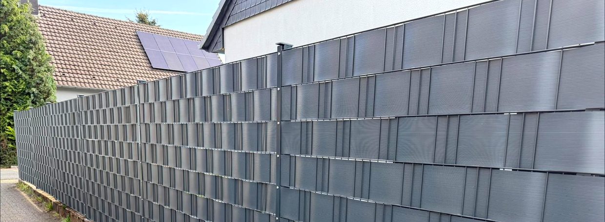 Langer Doppelstabmattenzaun mit anthrazitfarbenen Sichtschutzstreifen entlang einer Grundstücksgrenze